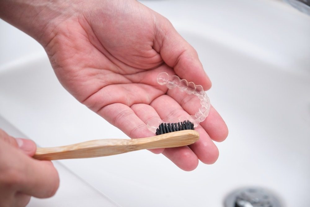 Hand holding clear aligner and toothbrush